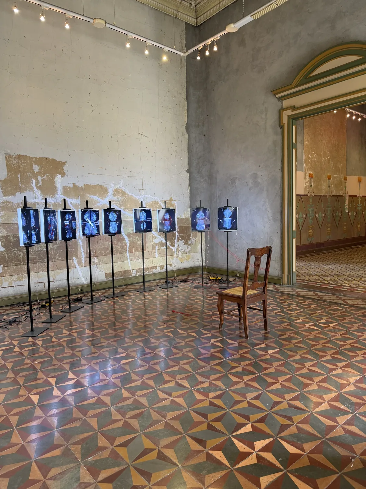 Montaje de la Sala 09 — Centro de Gravedad: instalación completa con las nueve mamografías en postes, la silla, los hilos rojos y el piso de mosaico