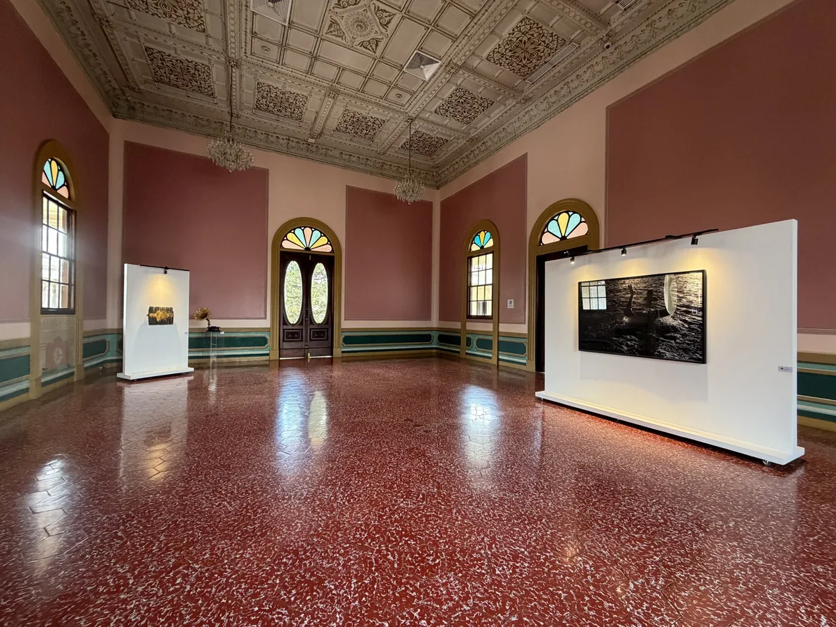 Montaje de la Sala 01 — El placer de estar aquí: el Salón Rosado con techo ornamentado, vitrales, lámparas, muros rosados y paneles con obras