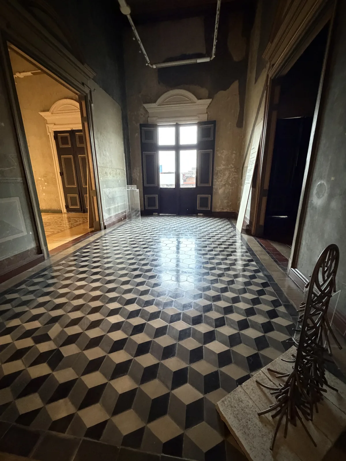 Montaje de la Sala 08 — Permanencia: vista del salón con obra escultórica en primer plano, piso de cubos, puertas y arquitectura del Palacio Nacional