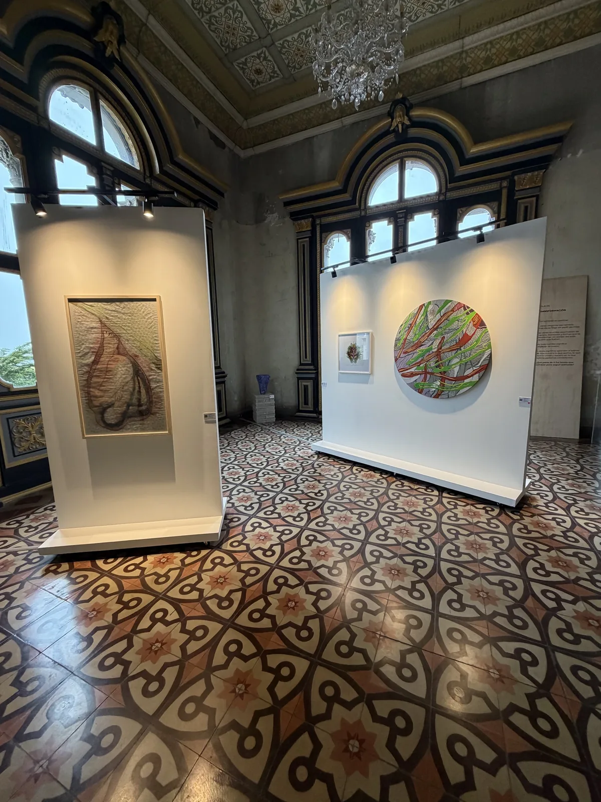 Montaje de la Sala 05 — Transformación: vista del salón con lámpara de araña, ventanales del Palacio Nacional y muros expositivos